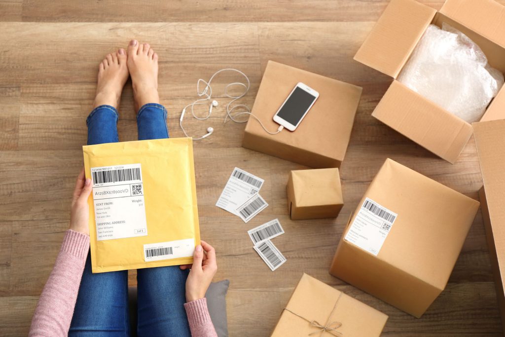 Girl's legs, envelope on them, phone, headphones, and boxes on her right