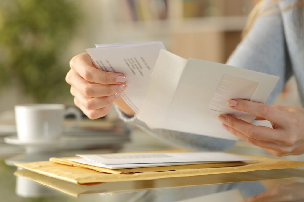 Woman holding an opened envelope, other envelopes on the table in front of her