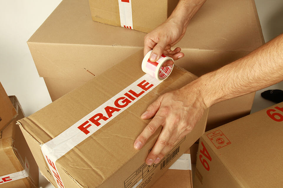 Man labeling a package with a tape with "fragile" written on it